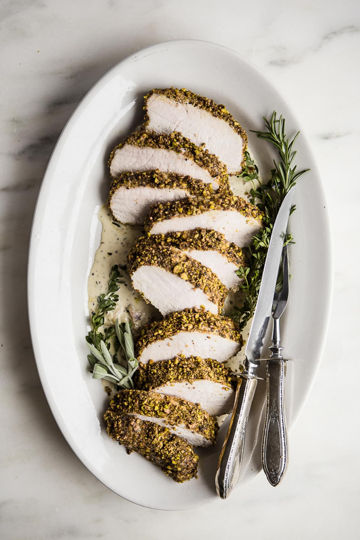 Pistachio Crusted Pork Tenderloin with White Wine Dijon Sauce on a plater with a carving knife