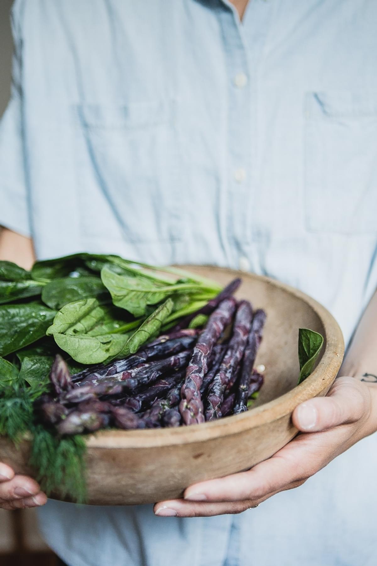 hands holding a bowl of purple asparagus, spinach and fresh dill.