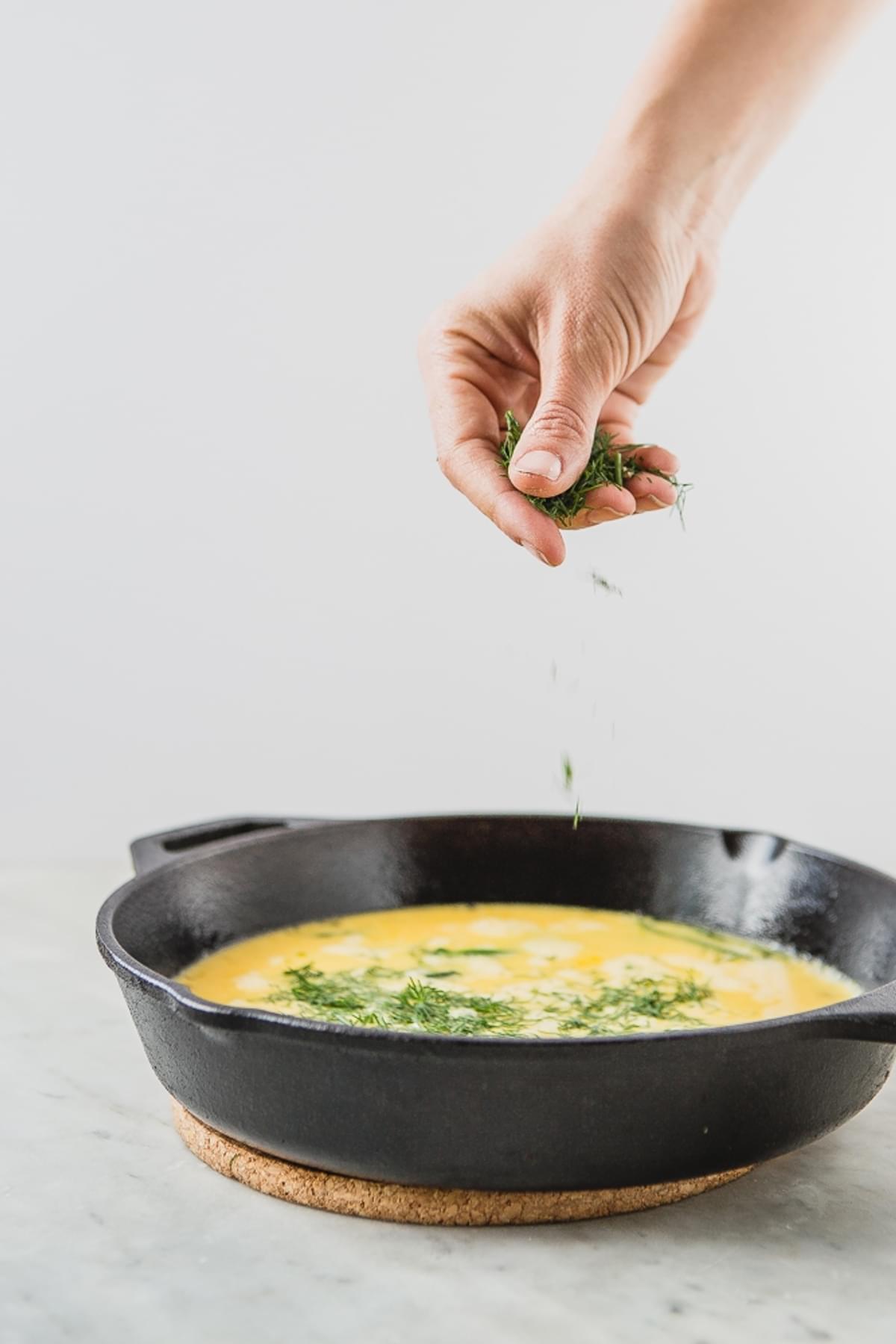 a hand sprinkling fresh minced dill onto Asparagus Frittata With Crème Fraîche and dill