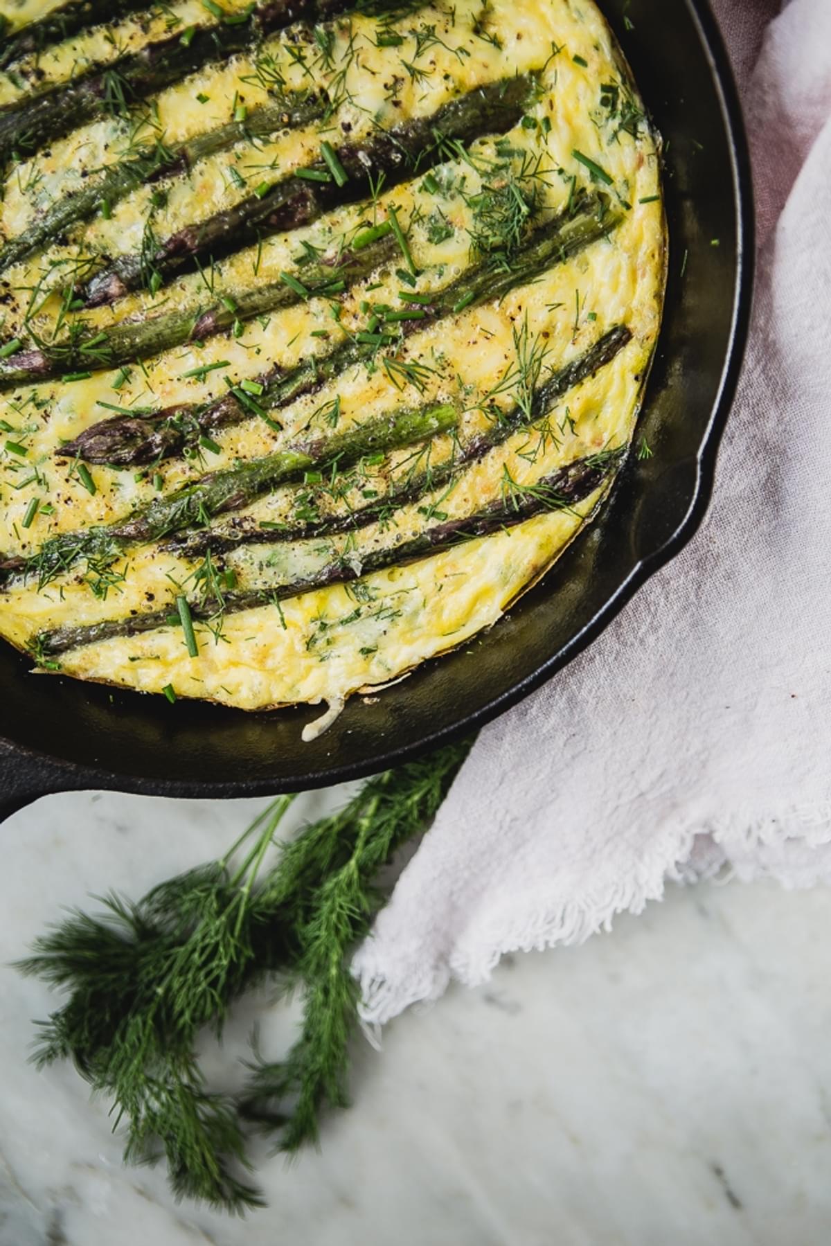Asparagus Frittata With Crème Fraîche and dill in a cast iron skillet with a linen