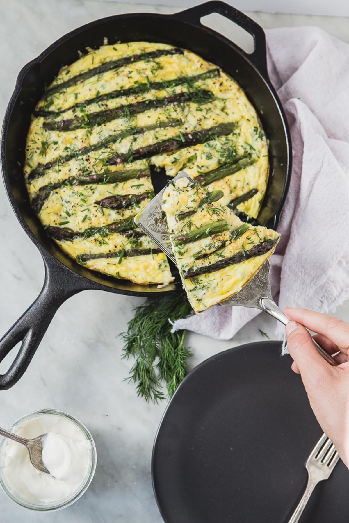 A hand dishing a piece of Spring Asparagus Frittata With Crème Fraîche