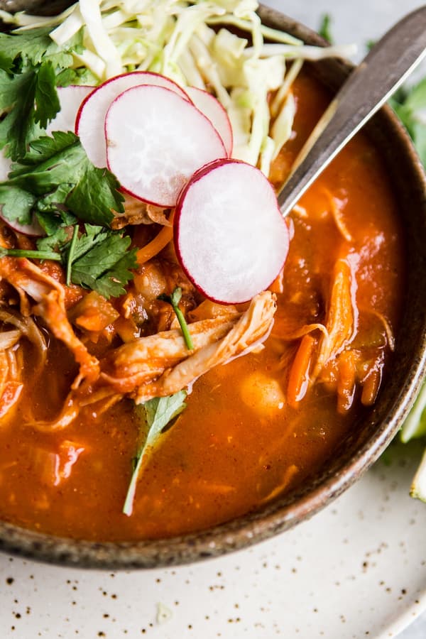 turkey pozole rojo in brown bowl topped with cilantro, radish slices and shredded cabbage