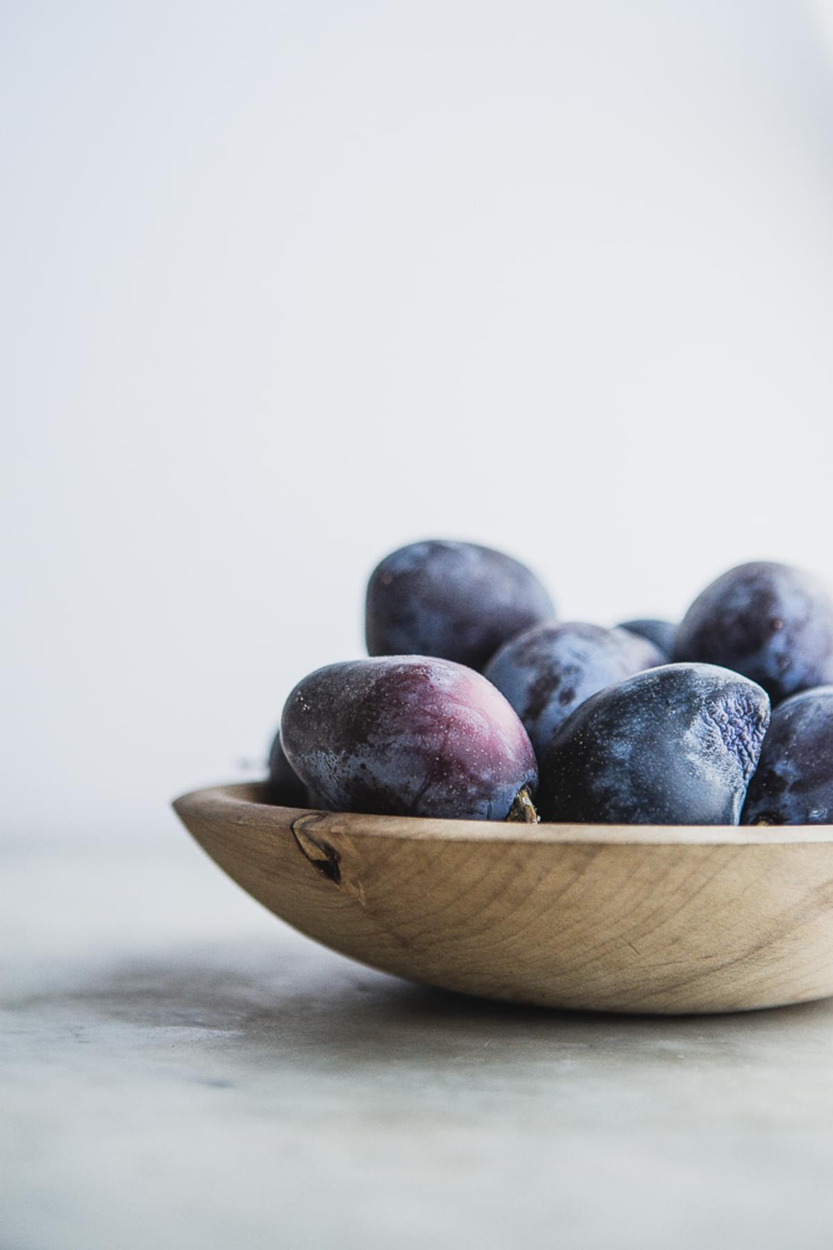 A wooden bowl filled with Italian plums