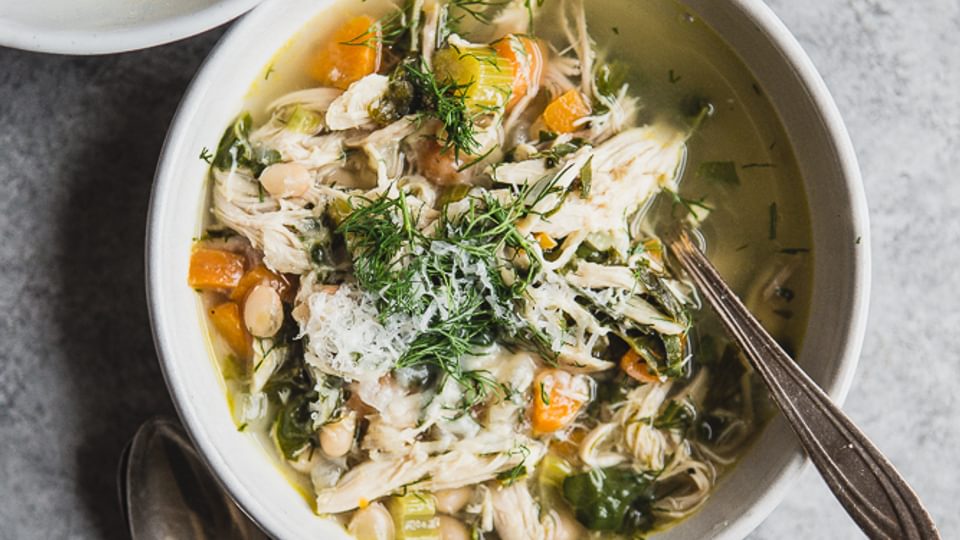 White Bean Chicken soup in a bowl with carrots fresh dill, chard, carrots and celery with a spoon.