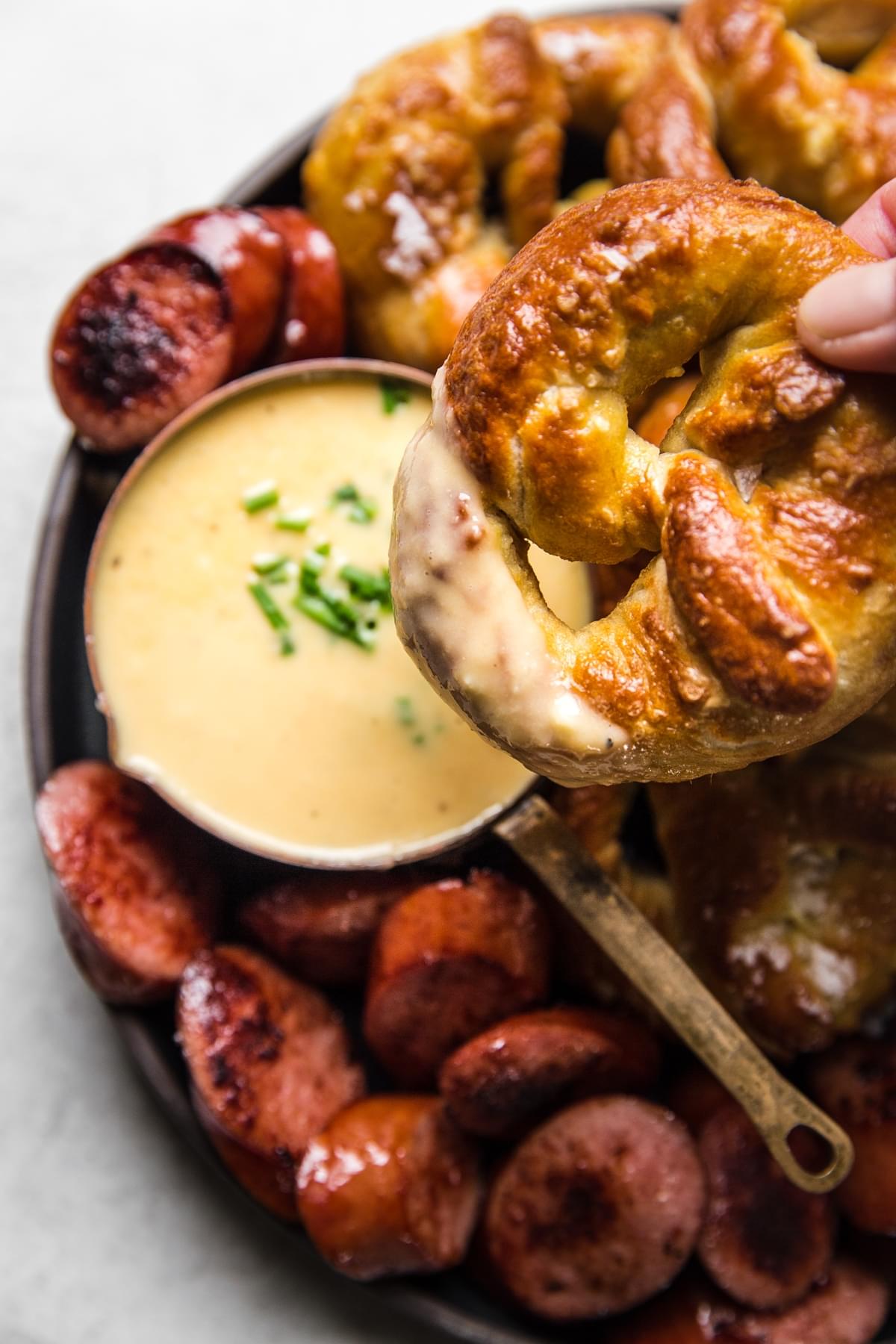 hand dipping a soft pretzel into a bowl of white cheddar beer cheese