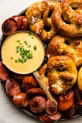 White cheddar beer cheese dip in a bowl next to soft pretzels and sausage slices