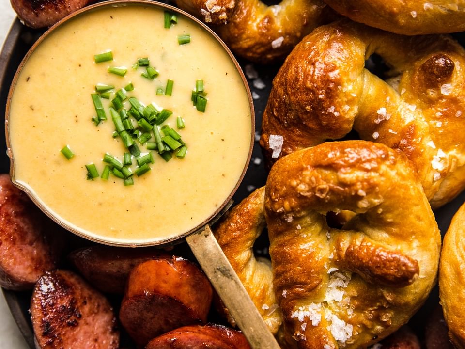 White cheddar beer cheese dip in a bowl next to soft pretzels and sausage slices