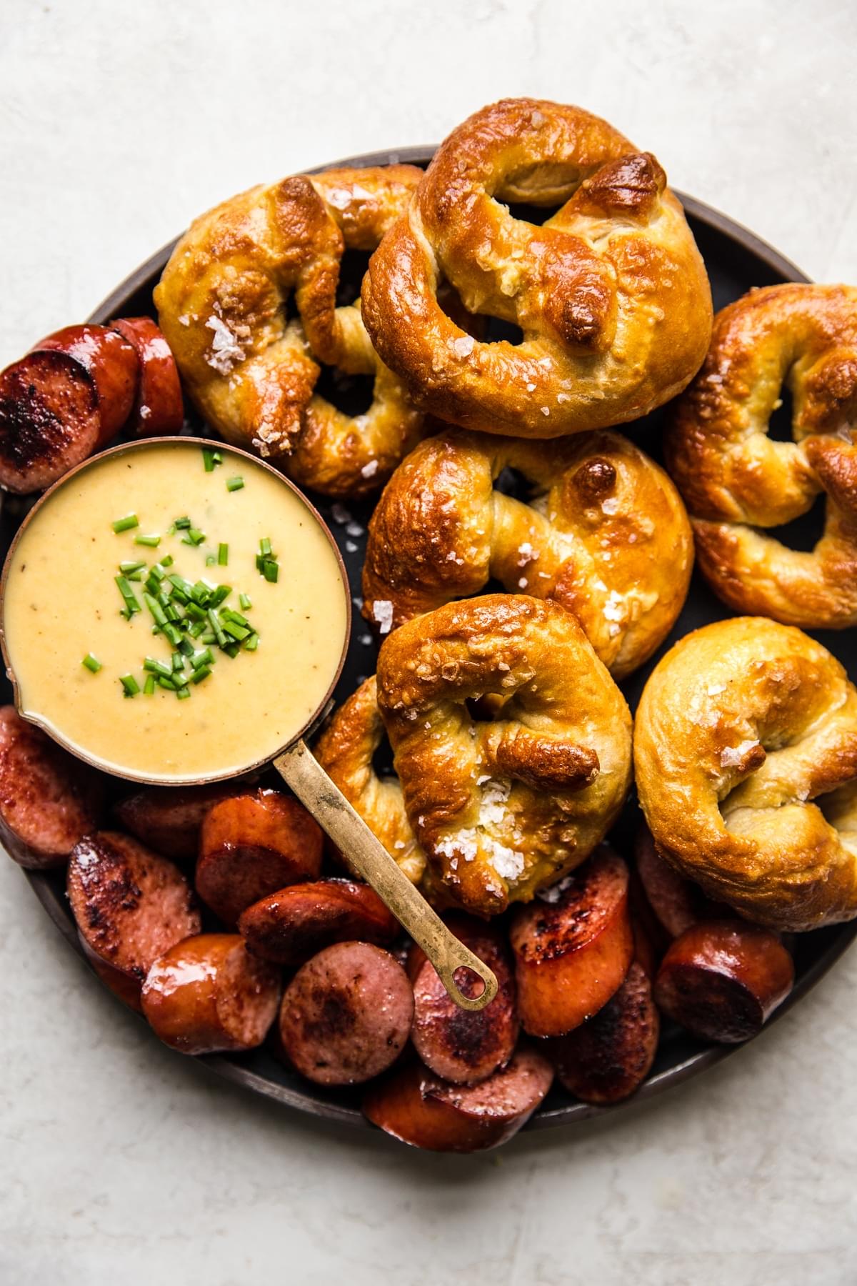 large plate with white cheddar beer cheese dip in small bowl next to soft pretzels and sausage slices