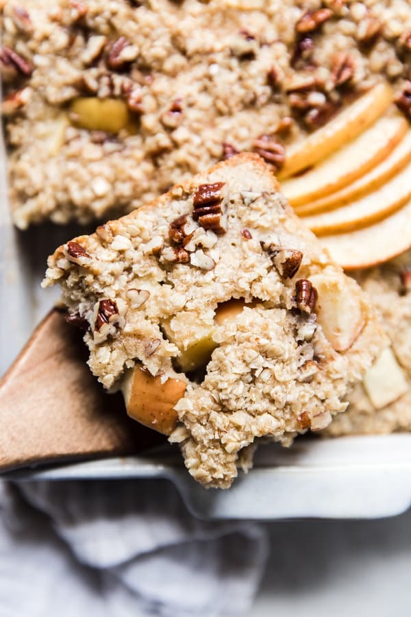 a piece of Baked Oatmeal With Apples, pecans and maple syrup on a wooden spoon.