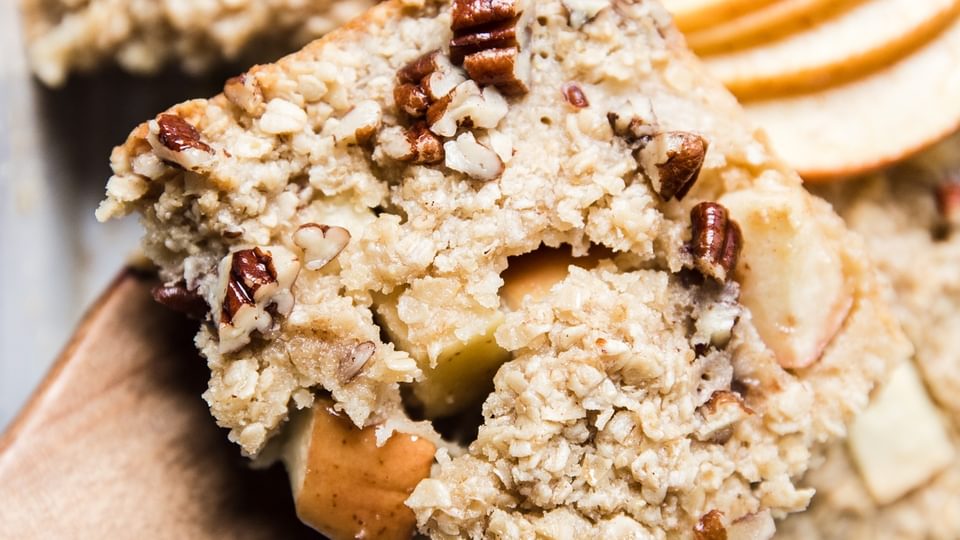 a scoop of Baked Oatmeal With Apples, pecans and maple syrup on a wooden spoon.