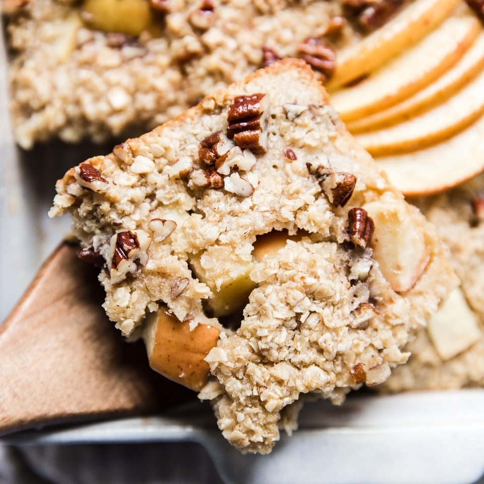 a piece of Baked Oatmeal With Apples, pecans and maple syrup on a wooden spoon.