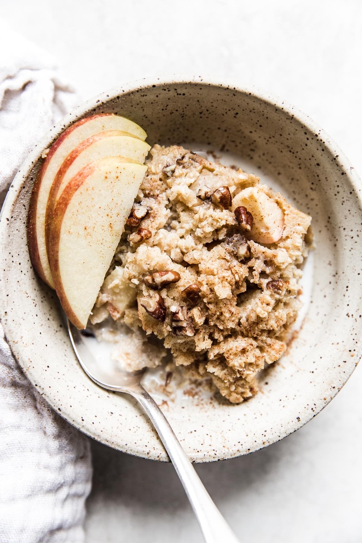 Baked Oatmeal With Apples in a bowl with apple slices, maple syrup and milk