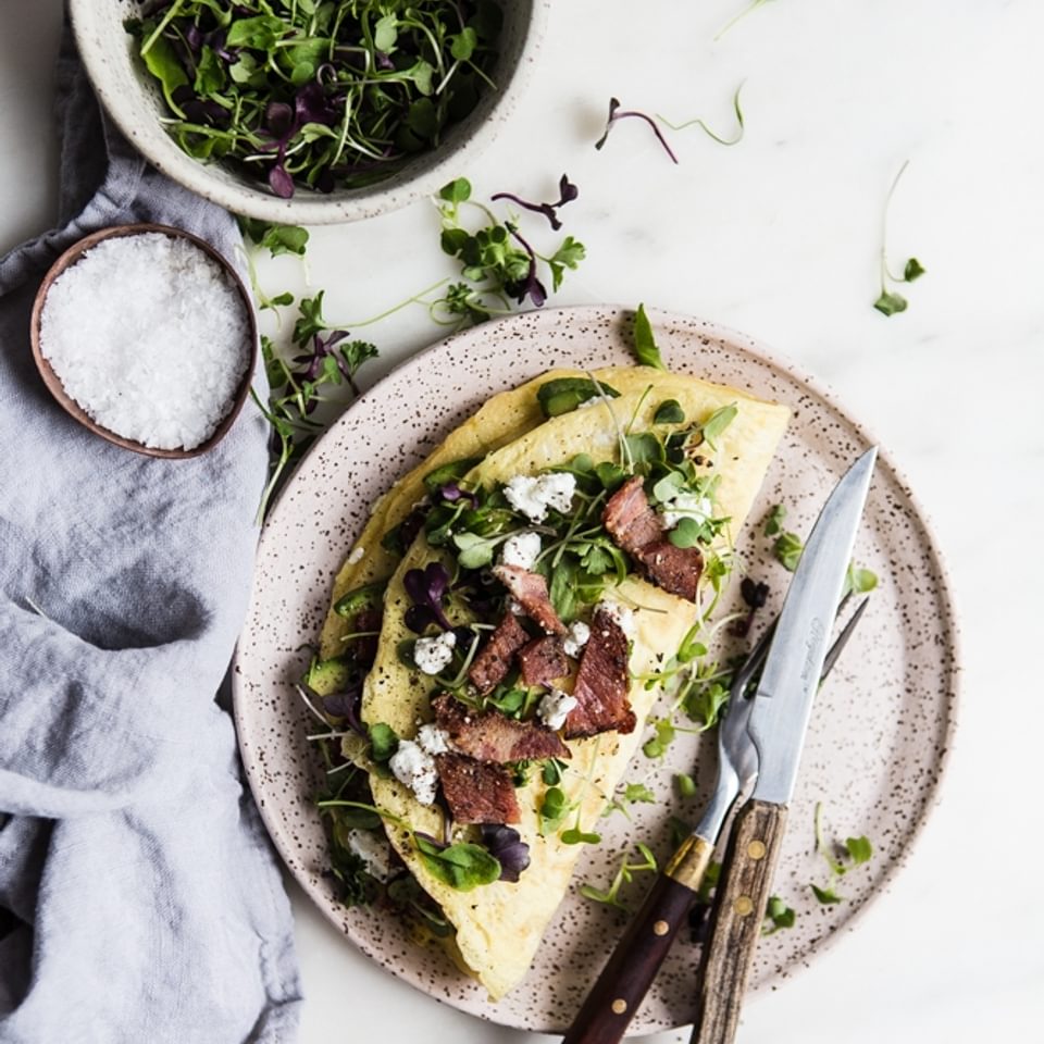 Avocado, Chèvre and Bacon Omelette on a plate with finishing salt in a small bowl