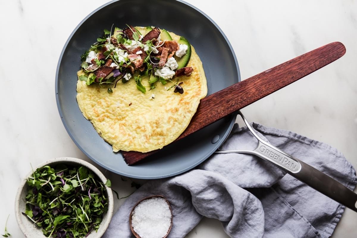 Avocado, goat cheese and Bacon Omelette in a frying pan with a wooden spoon