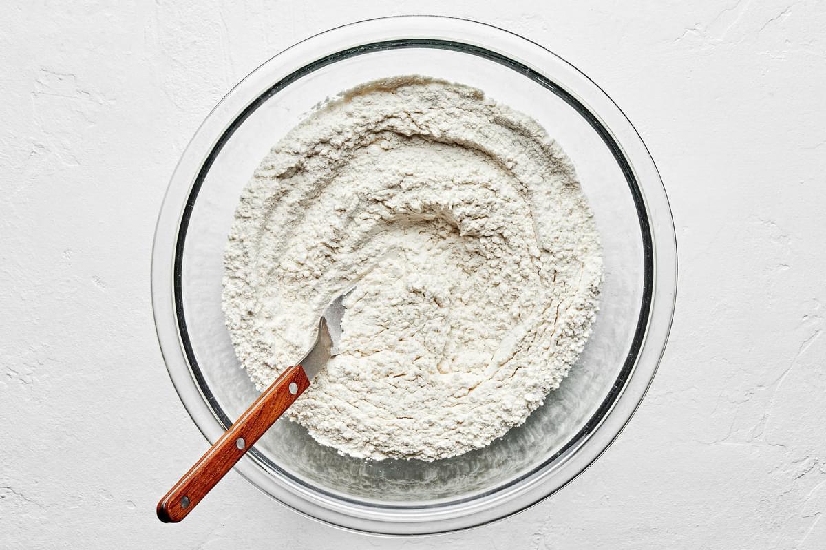 flour, baking soda and salt being whisked together in a mixing bowl