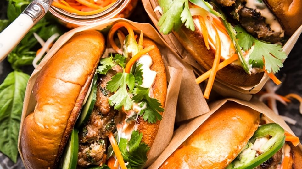 3 banh mi burgers on a plate with pickled carrots cilantro and jalapeños