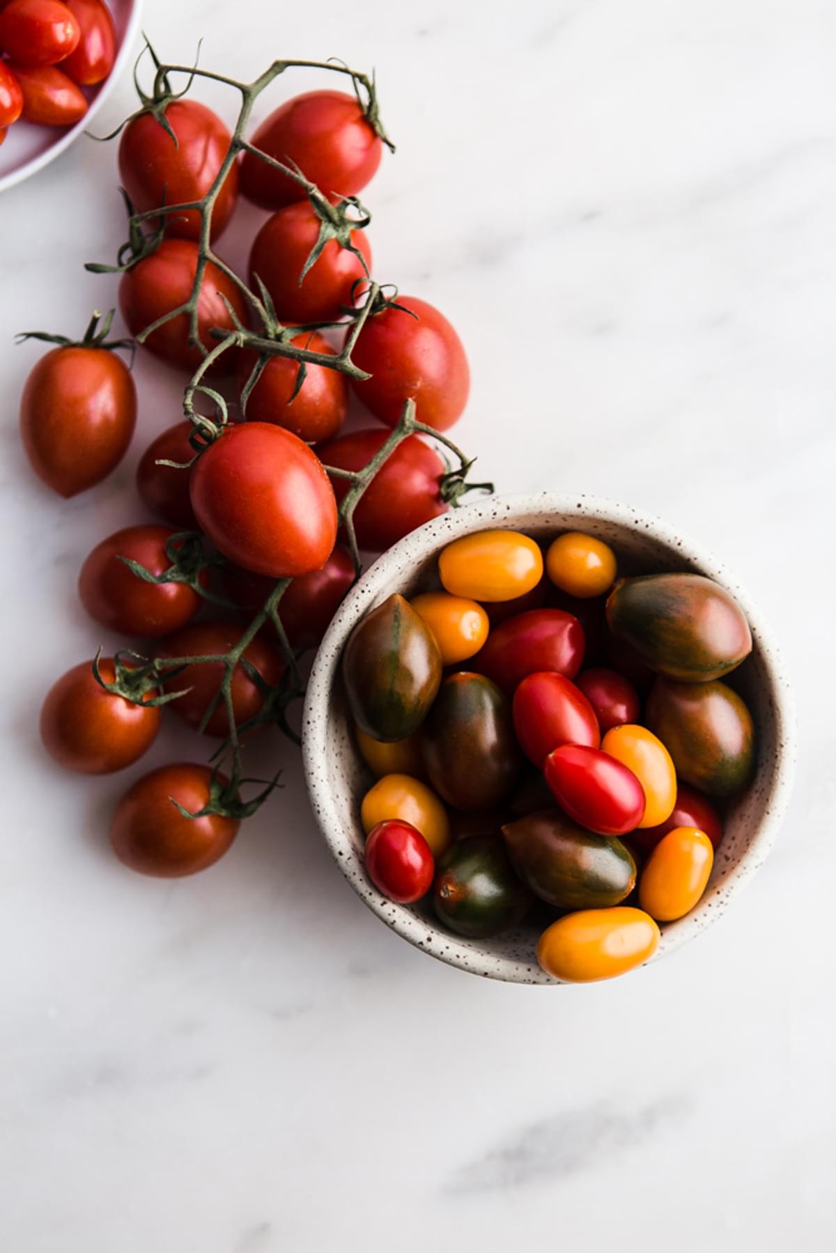 cherry tomatoes in a bowl and a few tomatoes on the vine