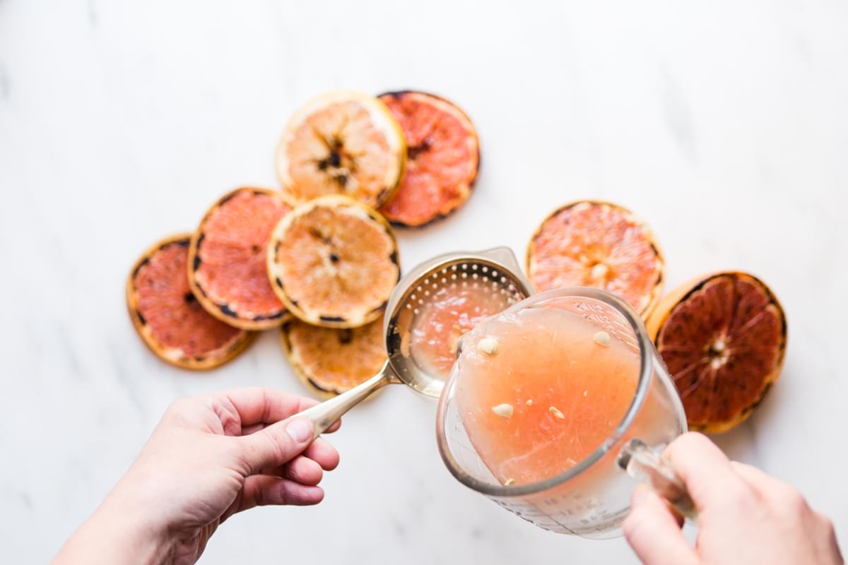 hand pouring grapefruit juice onto a strainer into a glass