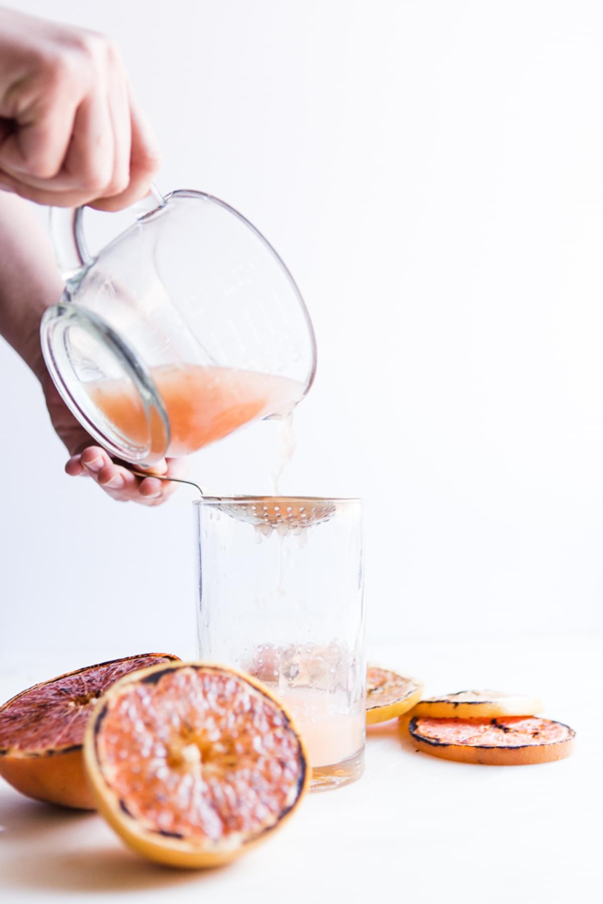 hands pouring grapefruit juice over a strainer into a glass