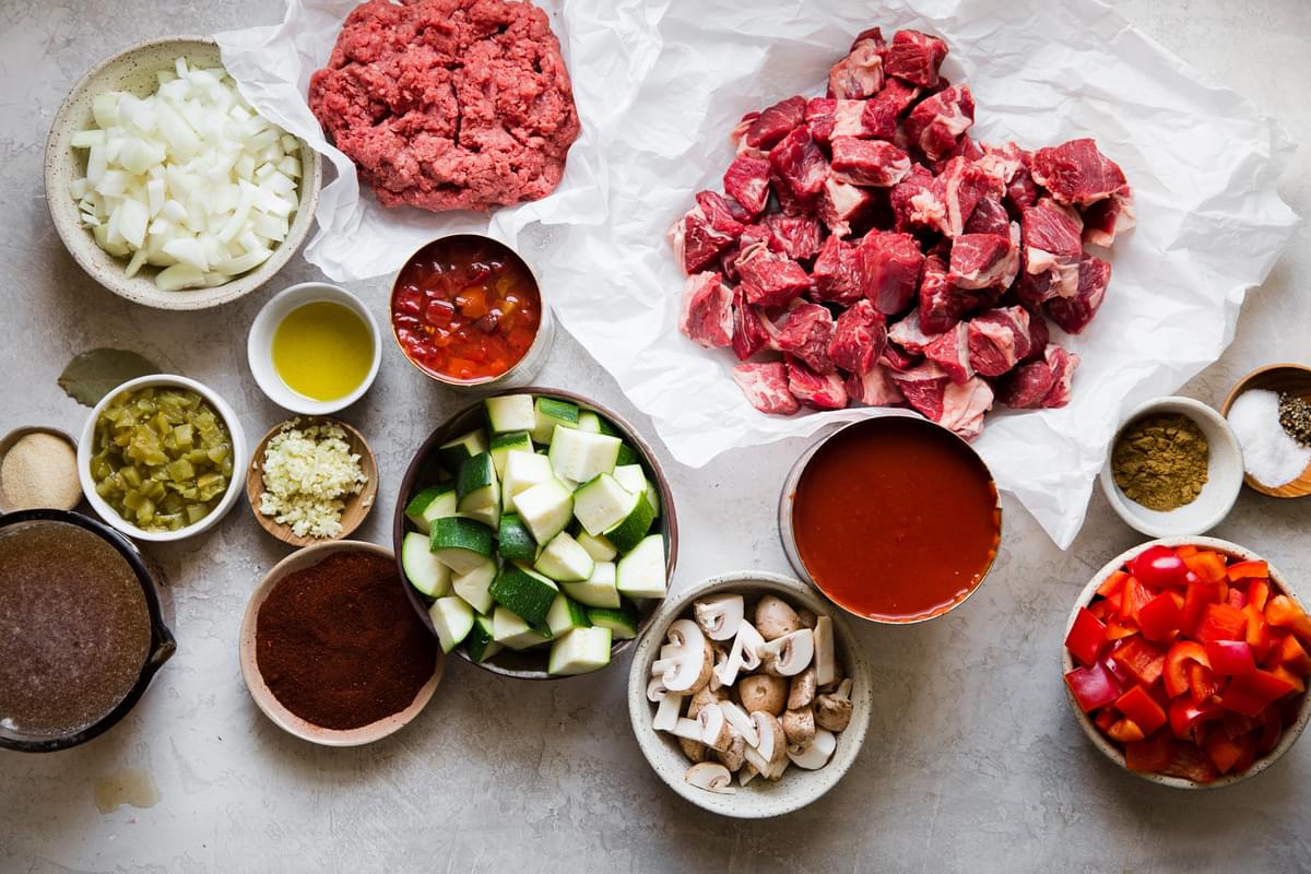 ingredients laid out for paleo chili: zucchini, mushrooms, bell peppers, chili powder, onion, ground beef, jalapeños