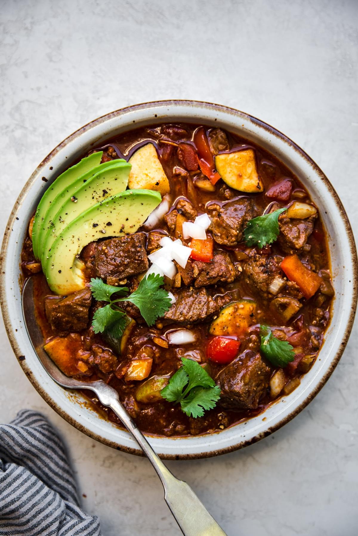 a bowl of homemade crockpot paleo chili in a bowl topped with avocado and cilantro