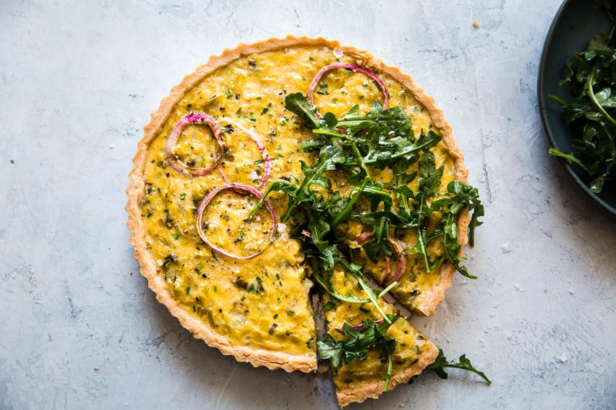 onion tart with a slice removed with and arugula salad