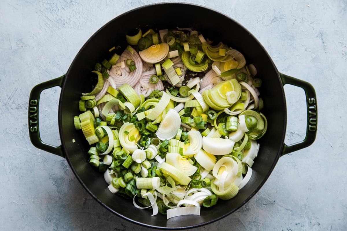 shallots, leeks, green onions and yellow onions being cooked in a pan with butter