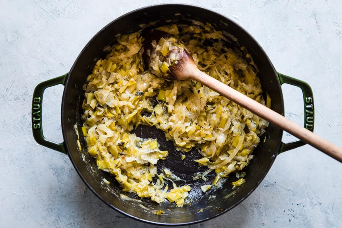 shallots, leeks, green onions and yellow onions caramelized in a pan with butter stored by a wooden spoon