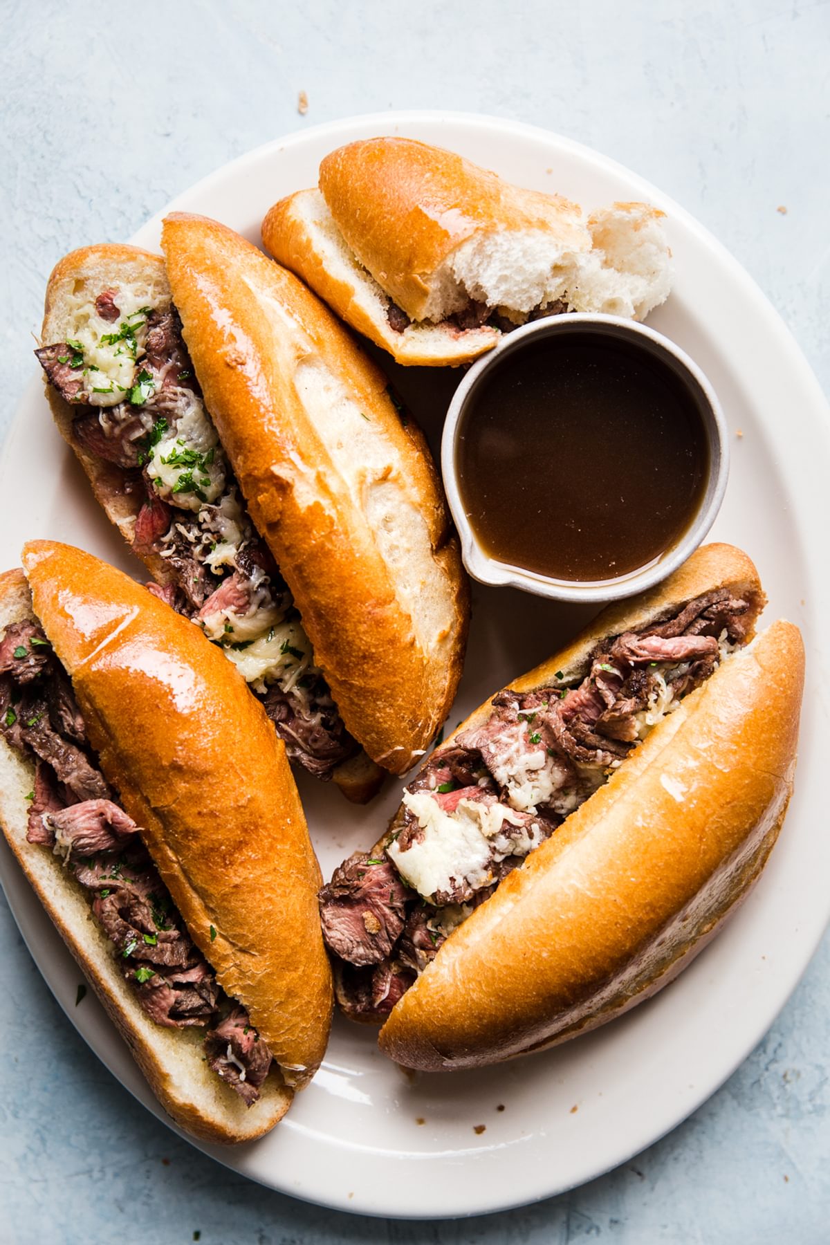 4 french dip sandwiches on a white plate with gruyere cheese and au jus sauce