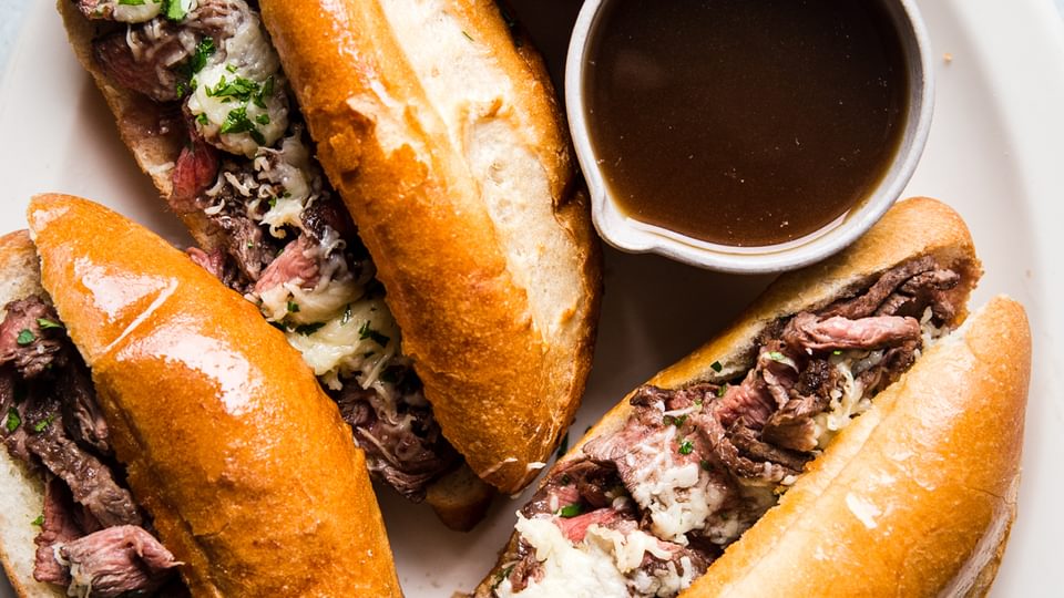4 french dip sandwiches on a white plate with gruyere cheese and au jus sauce