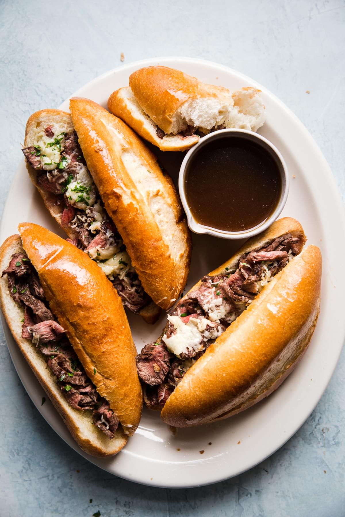 the best french dip sandwiches on a serving plater with thinly sliced steak, garlic butter, swiss cheese and au jus sauce