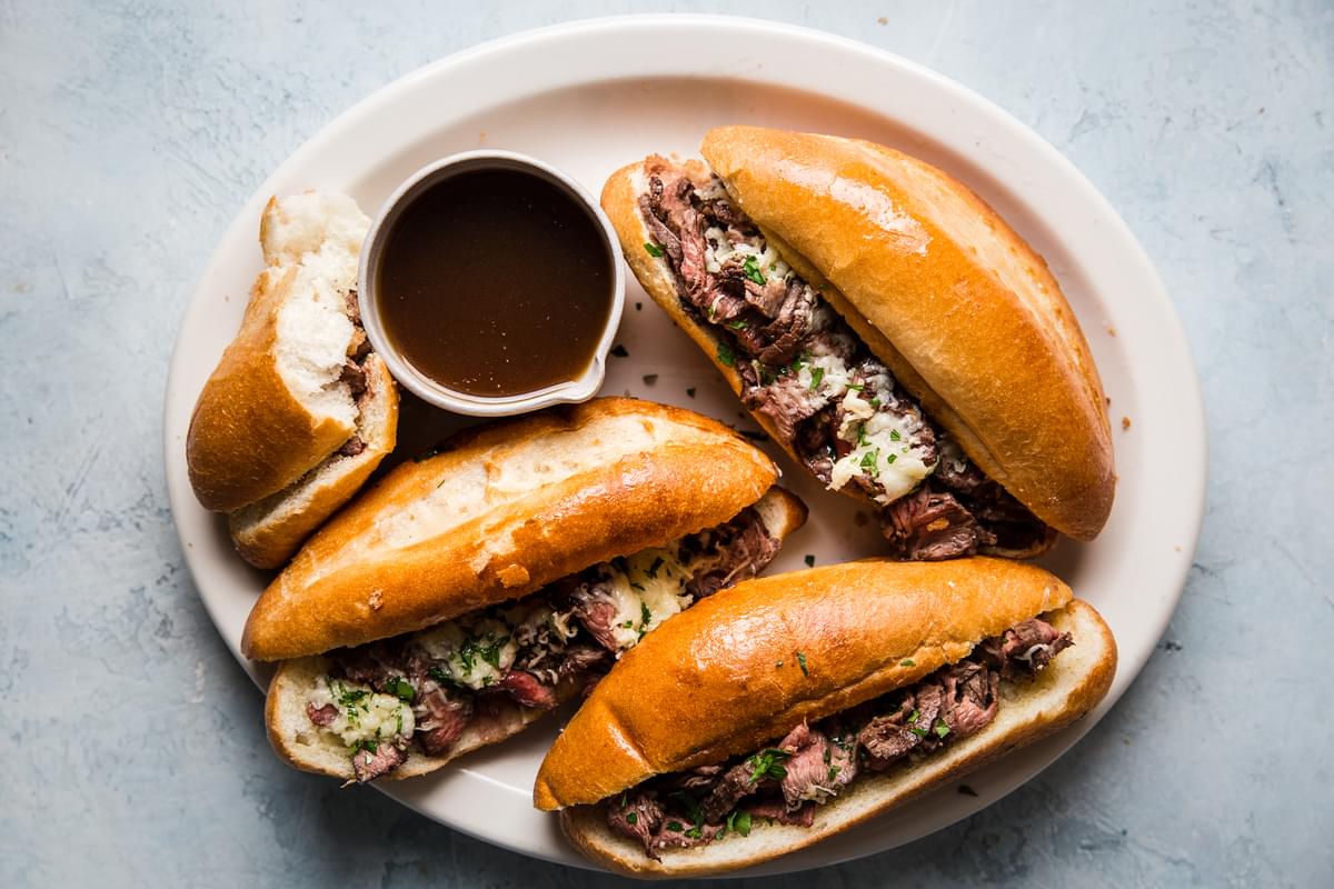 the best french dip sandwiches on a serving plater with thinly sliced steak, garlic butter, swiss cheese and au jus sauce