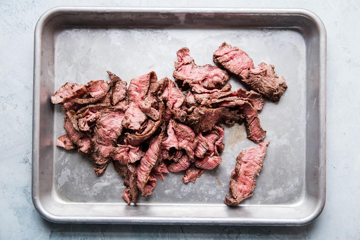 thin slices of flank steak on a baking sheet