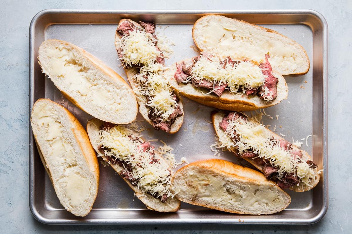 homemade french dip sandwiches open face on a baking sheet with thinly sliced steak, garlic butter and gruyere cheese