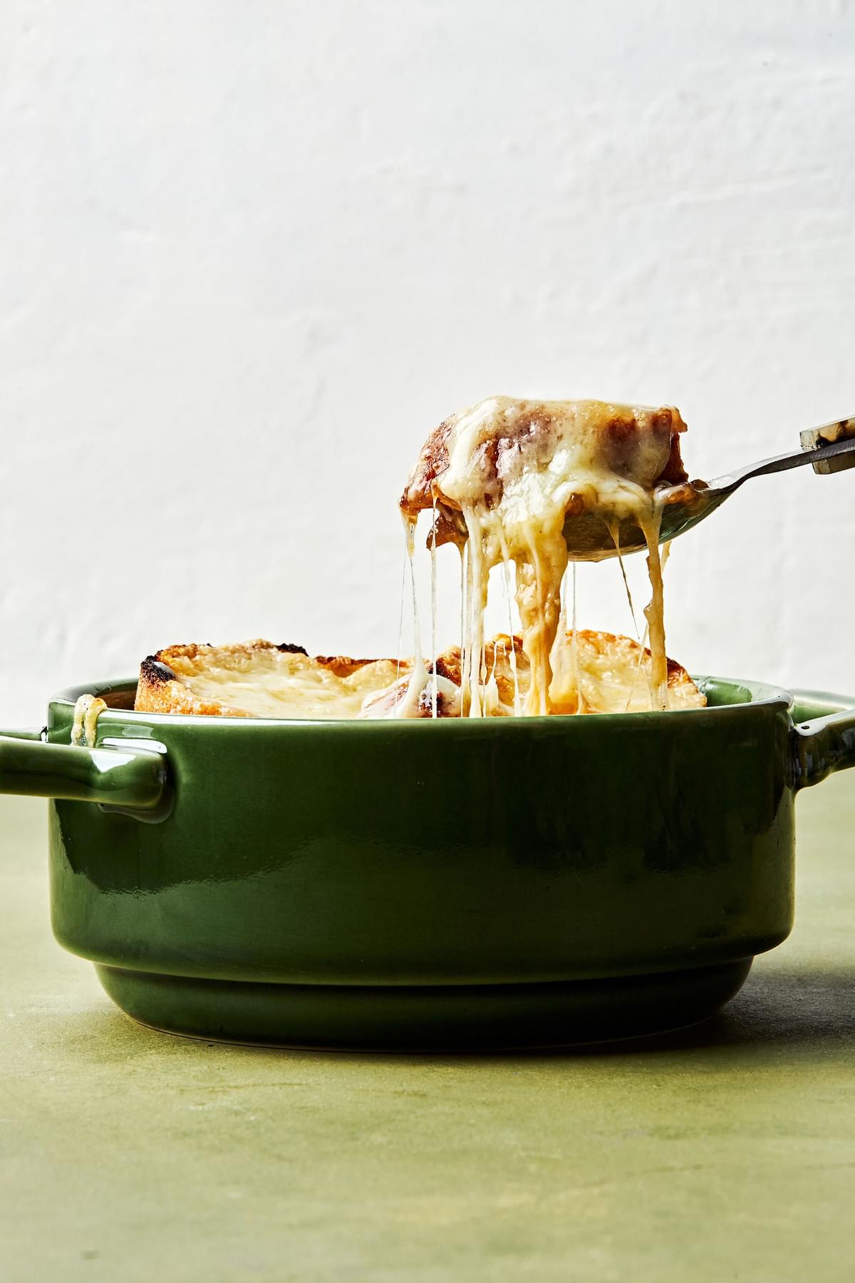 a bowl of homemade french onion soup topped with warm, bubbly Gruyère cheese with a spoon scooping out a bite