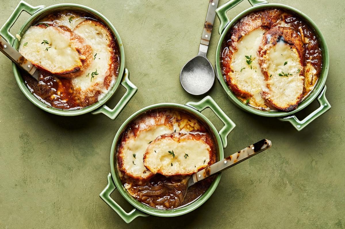 3 small oven proof bowls of french onion soup topped with sliced baguette and melted, bubbly Gruyère cheese