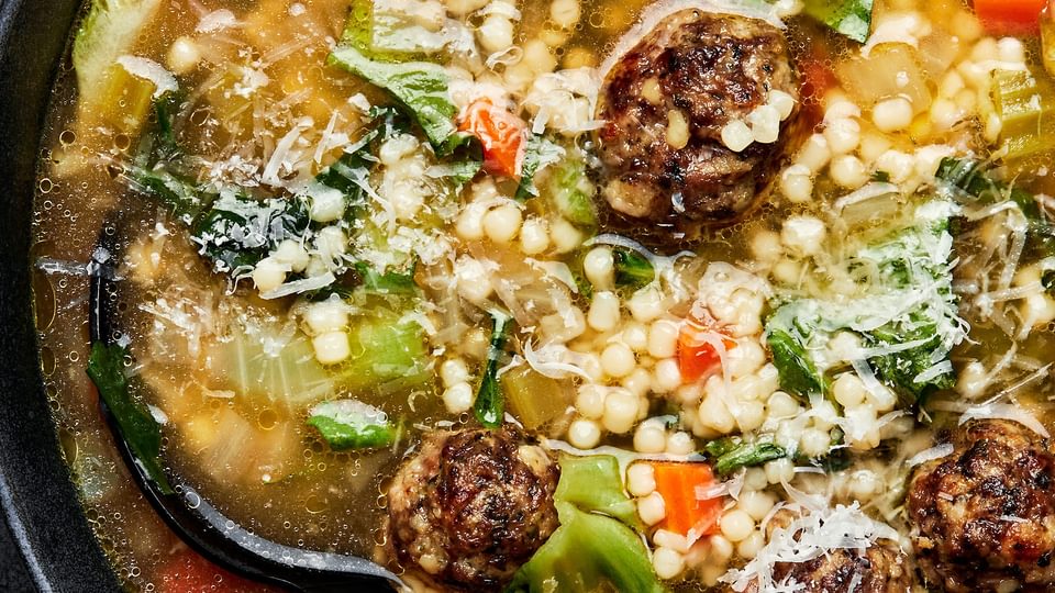 Italian wedding soup in a bowl with a spoon toped with parsley and Parmesan