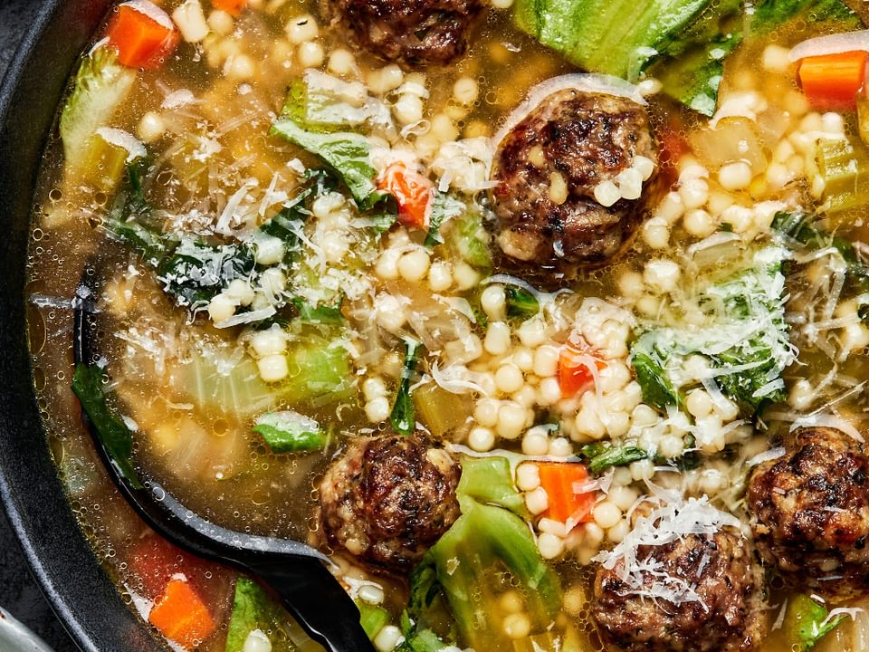italian wedding soup in a bowl with a spoon toped with parsley and a lemon wedge