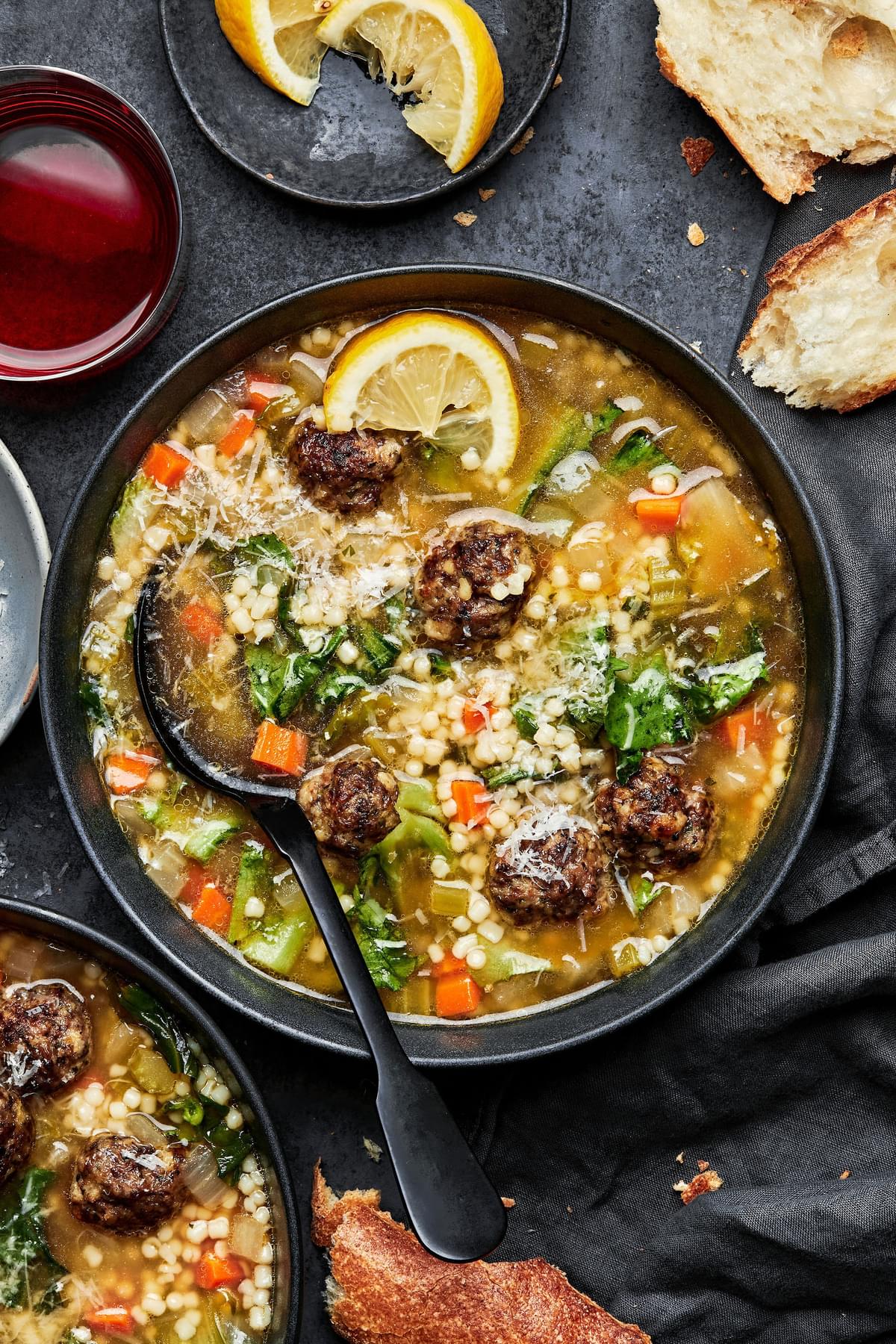 italian wedding soup in a bowl with a spoon toped with parsley and a lemon wedge