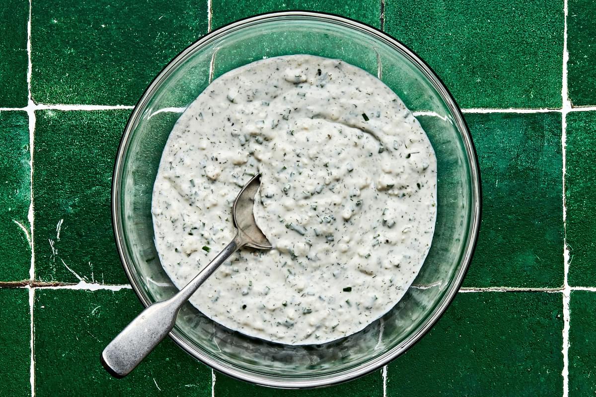creamy feta dressing in a bowl with a spoon made with feta, cream, lemon juice, chives, garlic, dill, sour cream & vinegar