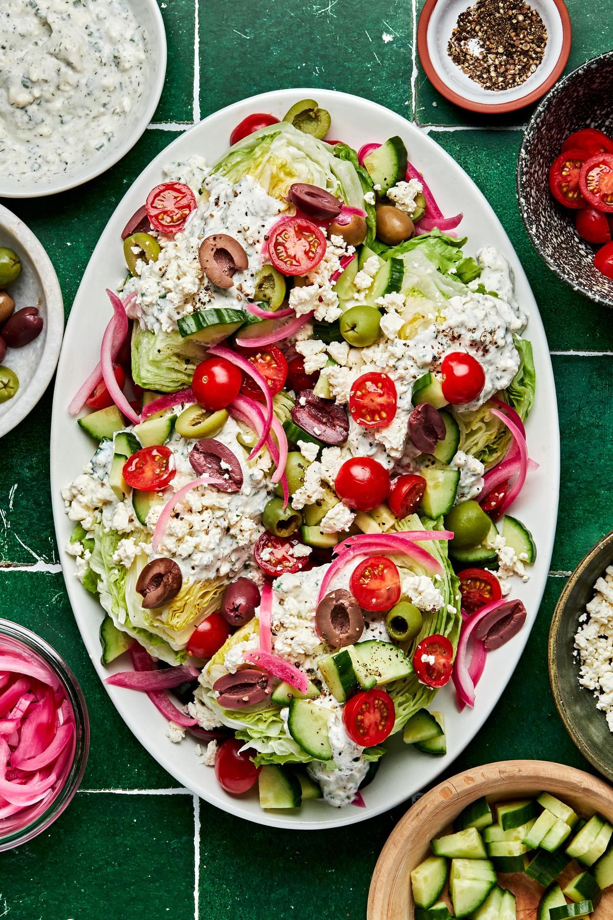 a platter of mediterranean wedge salads with tomatoes, cucumber, greek olives, pickled red onions and creamy feta dressing