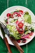 a mediterranean wedge salad with tomatoes, cucumber, greek olives, pickled red onions and creamy feta dressing on a plate