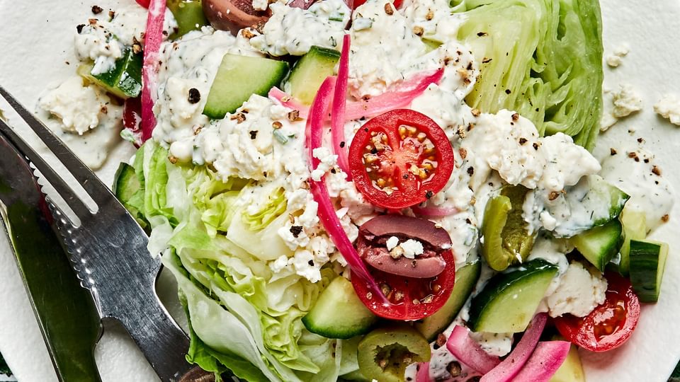 a mediterranean wedge salad with tomatoes, cucumber, greek olives, pickled red onions and creamy feta dressing on a plate