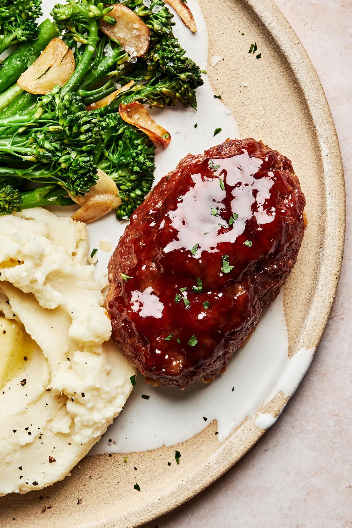 a plate with mini meatloaf with brown sugar sauce served with mashed potatoes and broccolini