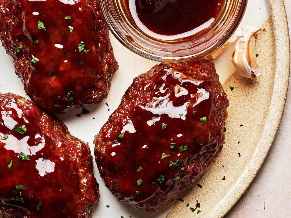 homemade mini meatloafs on a serving platter being brushed with a brown sugar sauce