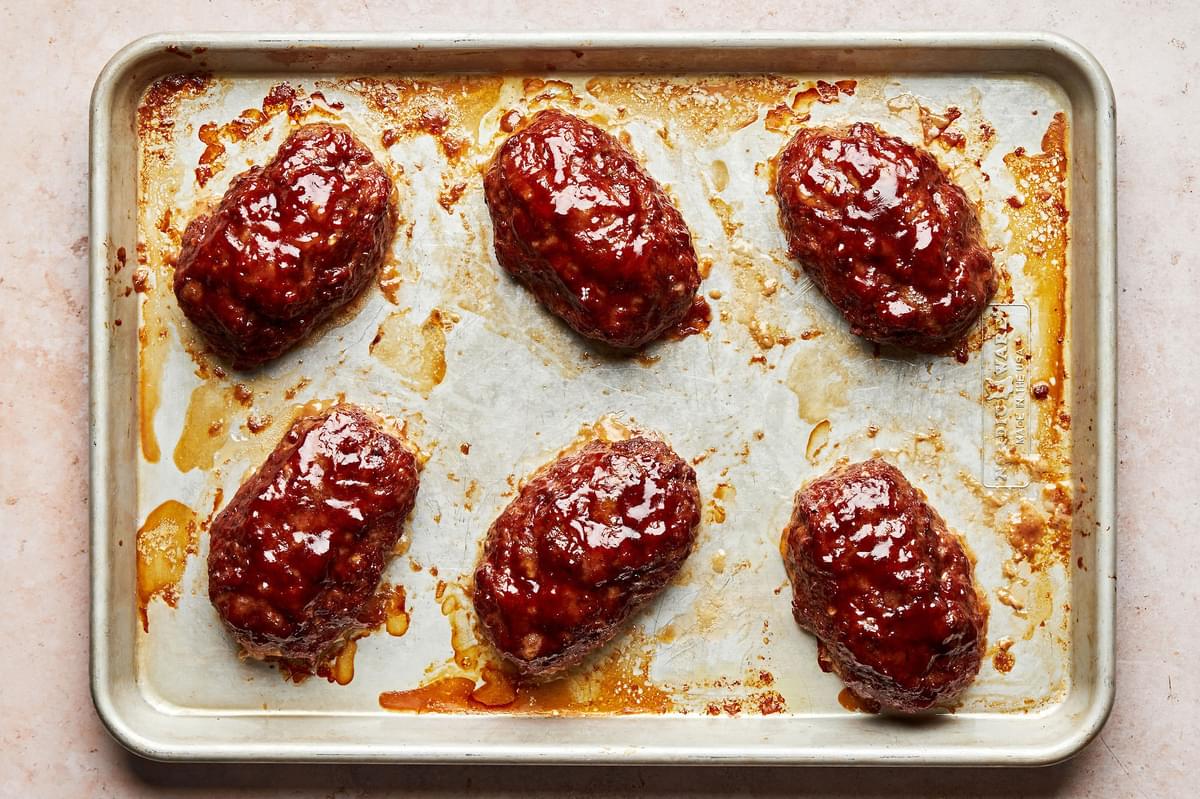 6 mini meatloaves on a baking sheet just out of the oven made with ground beef, ground pork, breadcrumbs and spices