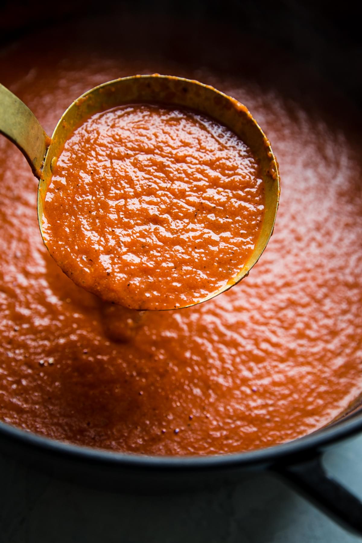 roasted red pepper soup in a ladle over a pot of soup