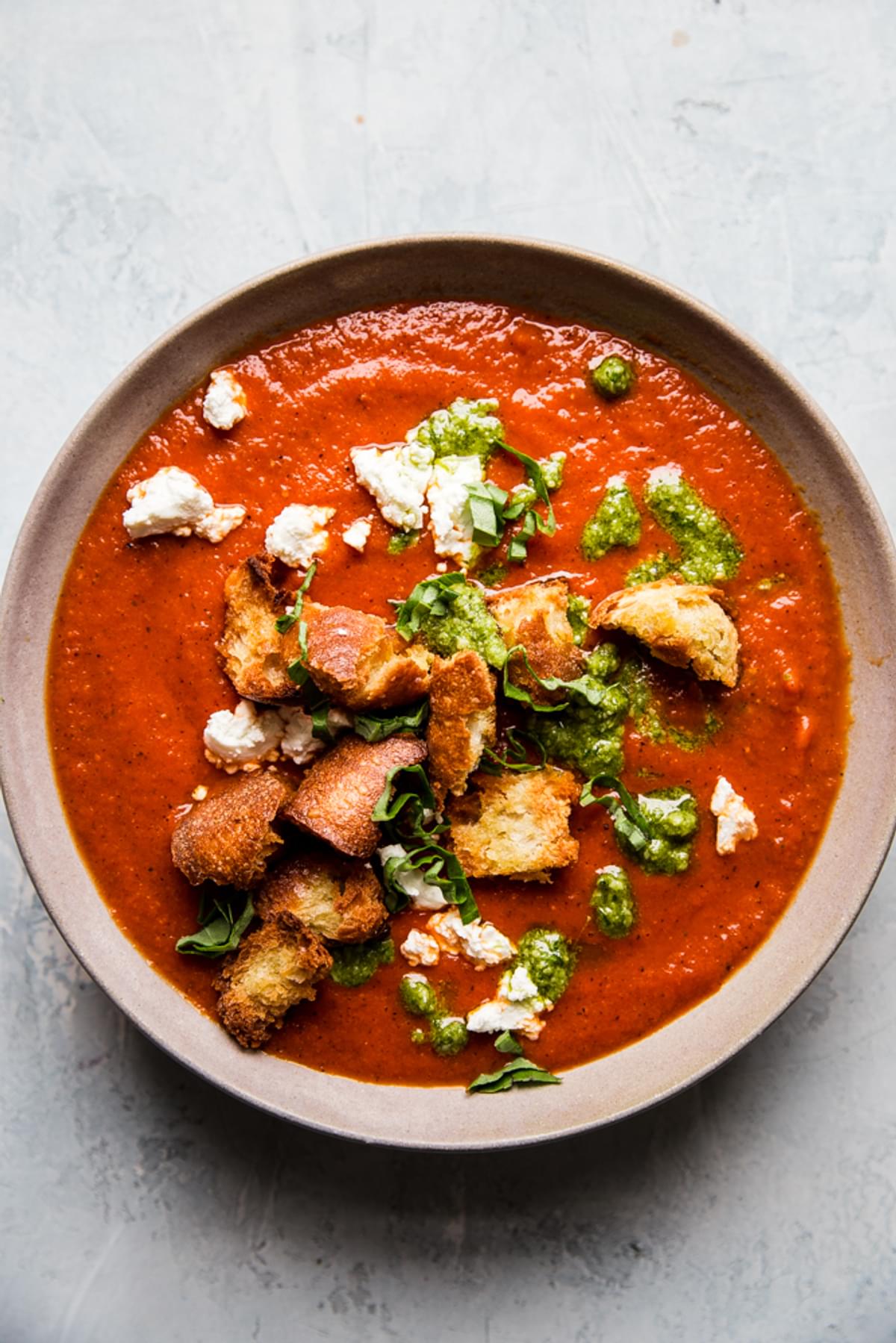 Roasted red pepper soup in a bowl with croutons, goat cheese and pesto