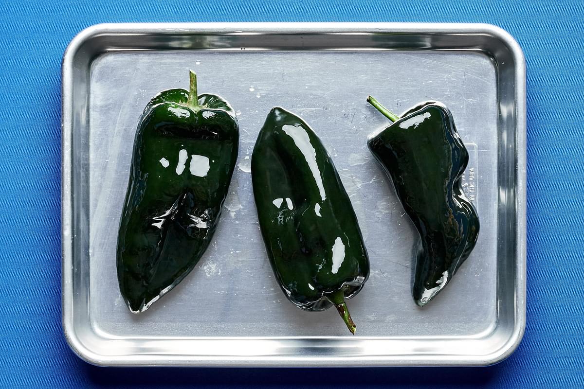 poblano peppers brushed with olive oil on a baking sheet ready to be broiled in the oven