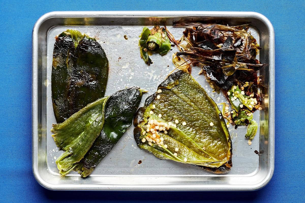 roasted poblano peppers on a baking sheet with the skins, cores, stems and seeds being removed